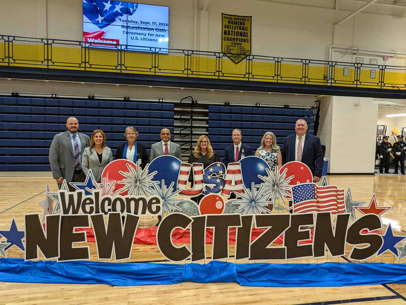 Group standing behind a sign that reads "Welcome New Citizens"
